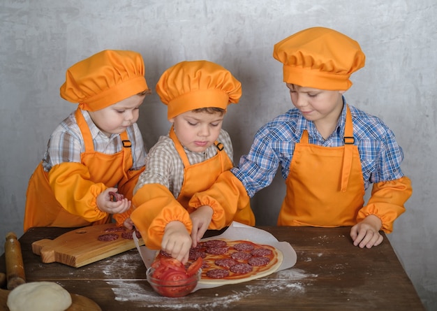 i fratelli aiutano la mamma a cucinare la pizza con salsiccia e formaggio