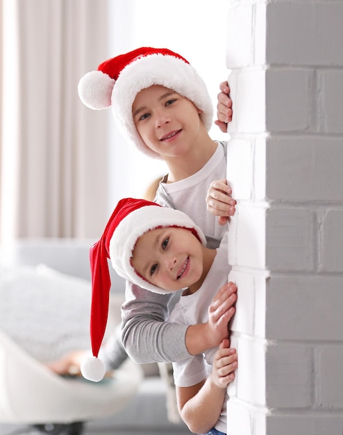 I fratelli con i cappelli di Babbo Natale guardano attraverso un muro di mattoni