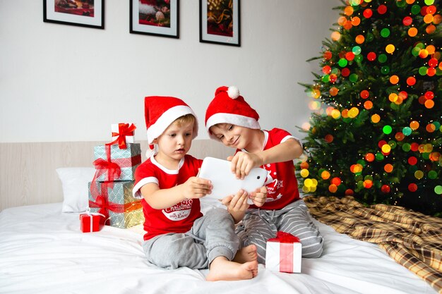 I fratelli con i cappelli di Babbo Natale guardano un tablet e scelgono i regali