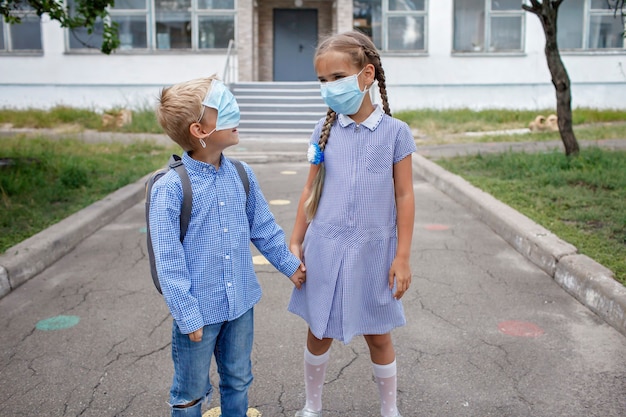 I fratelli di ritorno a scuola con gli zaini nelle maschere mediche rimangono vicino alle porte prima del primo giorno offline