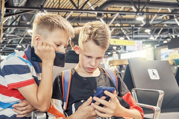 I fratelli giocano e condividono interessi utilizzando gli smartphone nella sala d'attesa con le poltrone in aeroporto