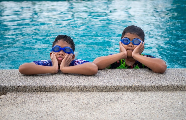 I fratelli indossano costumi da bagno e occhiali Sorridono mentre sono appollaiati sul bordo della piscina