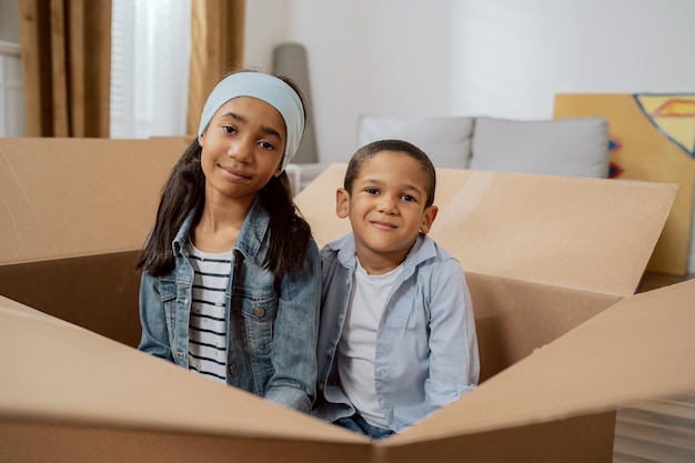 I fratelli sorridenti si siedono in una scatola di cartone vuota durante un trasloco i bambini si nascondono dai loro genitori