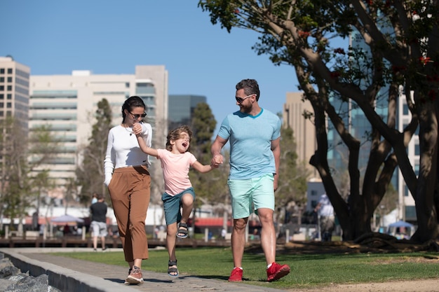 I genitori con il figlio che camminano nella famiglia della città che fanno una passeggiata sulla strada all'aperto contro il paesaggio della città