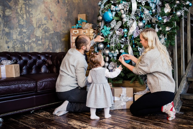 I genitori con la figlia decorano l'albero di Natale a casa. Famiglia, natale, vacanze invernali e concetto di persone. La famiglia con il bambino celebra le vacanze invernali.