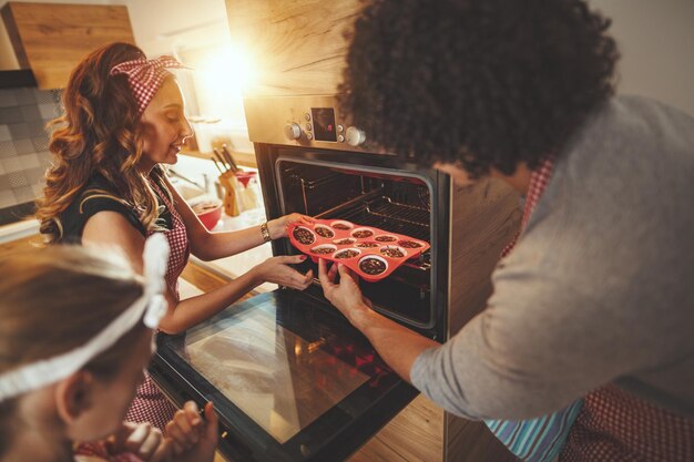 I genitori felici e la loro figlia mettono i biscotti in forno da cuocere, prendendosi gioco.