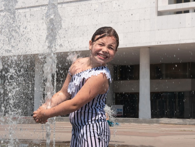 I getti d'acqua della fontana eruttano da terra, una ragazza gioiosa schiva l'acqua