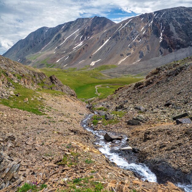 I ghiacciai si sciolgono, l'acqua scorre nella valle. Il pittoresco paesaggio dell'altopiano con il fiume di montagna nella valle tra le alte montagne con la neve. Splendida vista alpina sulla variegata valle di montagna, vista sulla piazza