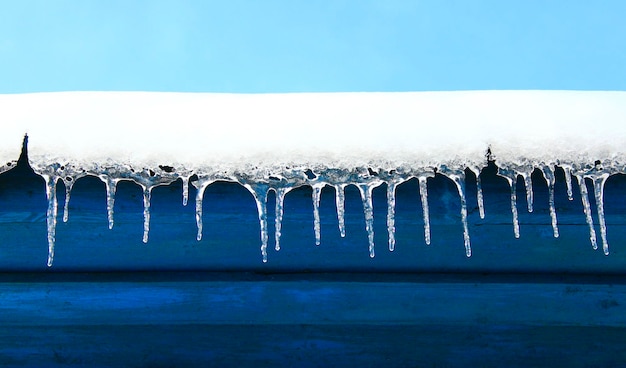 I ghiaccioli pendono da sotto il tetto della casa Modello invernale congelato in fila