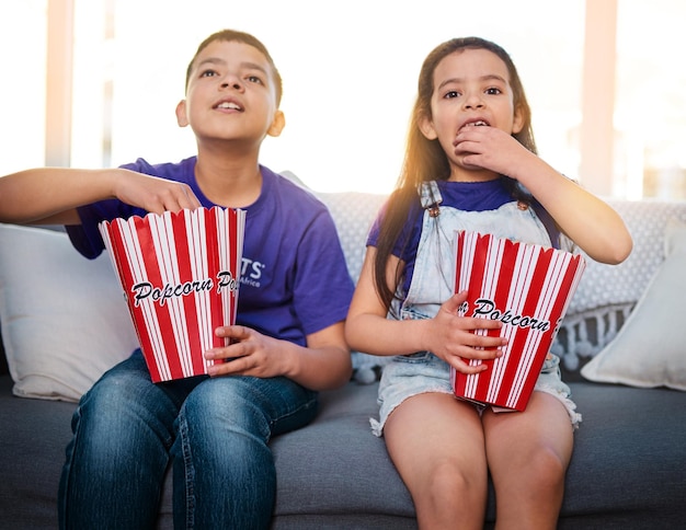 I giorni del cinema sono sempre i migliori Scatto di due bambini piccoli seduti su un divano che mangiano popcorn mentre guardano film a casa