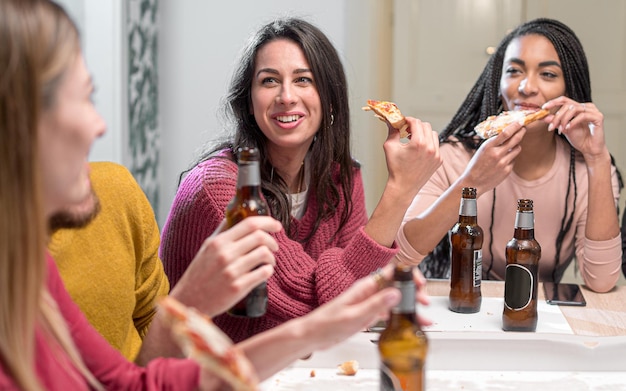 I giovani a casa si divertono a fare una pizza party insieme. Amici multirazziali della generazione millenaria che bevono birre e mangiano fette di pizza