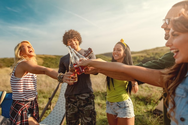 I giovani amici felici si godono una giornata di sole nella natura. Stanno facendo tintinnare bottiglie di birra, ridendo e parlando felici di stare insieme.