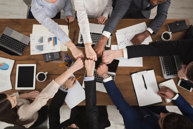 I giovani che uniscono i pugni come simbolo di unità e realizzazione, vista dall'alto. Gruppo di persone pugno urto assemblare insieme sul posto di lavoro. Concetto di lavoro di squadra, copia spazio nel mezzo