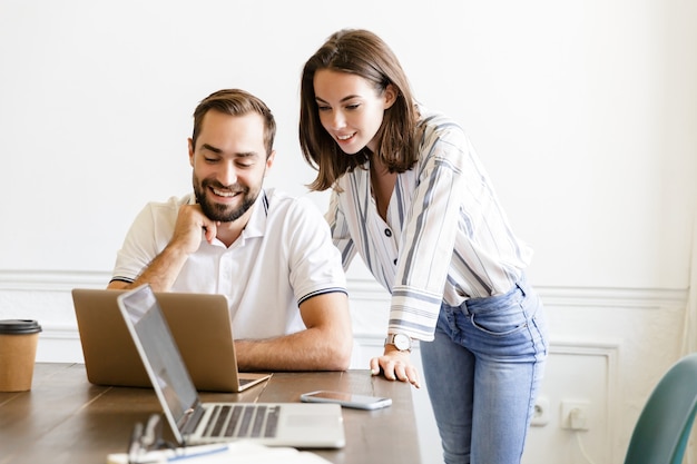 i giovani colleghi sorridenti felici delle coppie lavorano con il computer portatile all'interno in ufficio che parlano con a vicenda.