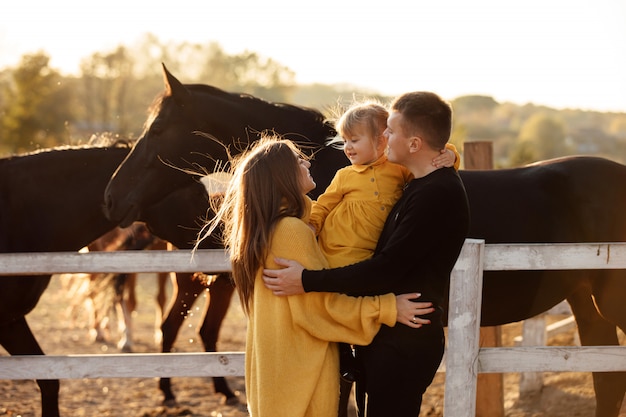 I giovani genitori camminano con la piccola figlia vicino ai cavalli nella sosta di autunno.