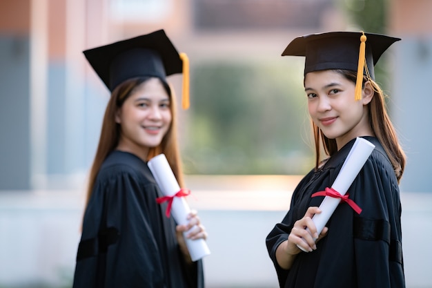 I giovani laureati universitari felici della donna asiatica in abito di graduazione e mortarboard tengono un certificato di laurea celebrano il successo di istruzione nel campus universitario. Istruzione foto d'archivio