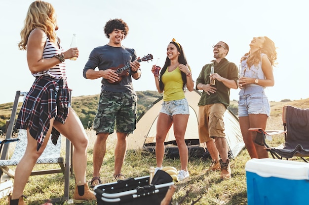 I giovani si divertono in campeggio nella natura. Stanno riposando, ridendo e cantando con la musica dell'ukulele, felici di stare insieme.