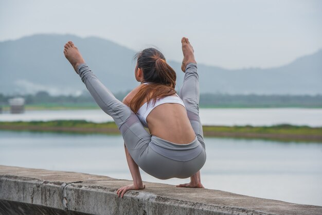 I giovani sport donna che fa l&#39;yoga sul lago con sfondo di montagna.