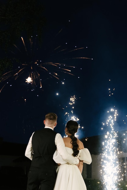 I giovani sposi stanno vicino all'arco delle nozze di notte con le luci del fumo e le sagome dei fuochi d'artificio degli sposi novelli