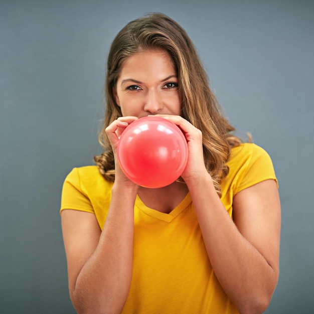 I gonfiatori si gonfiano Inquadratura di una giovane donna che gonfia un palloncino su uno sfondo grigio