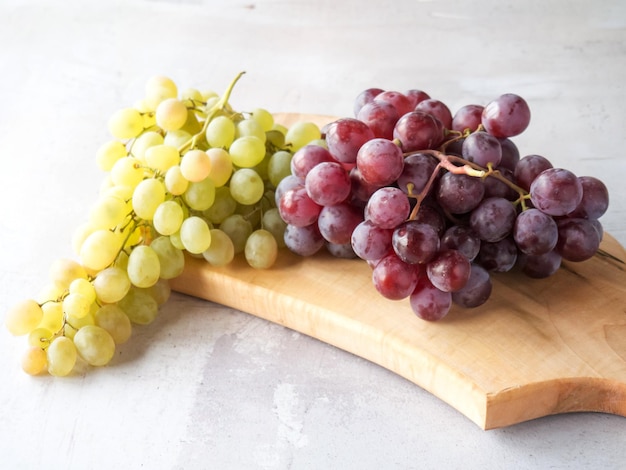 I grappoli di uva bianca e rossa giacciono su un tagliere su uno sfondo chiaro