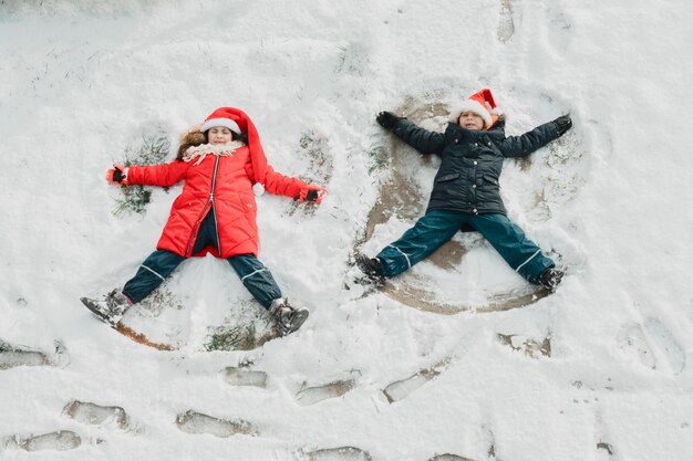 I graziosi bambini fanno l'angelo della neve per terra