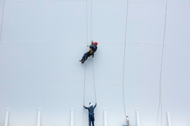 I lavoratori di sesso maschile controllano la fune verso il basso altezza del serbatoio accesso alla fune ispezione dello spessore della lamiera di rivestimento del serbatoio di stoccaggio del lavoro di sicurezza in altezza.