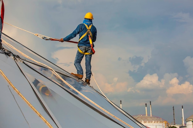 I lavoratori di sesso maschile hanno accesso alla fune di sicurezza in altezza che si collegano con un'imbracatura di sicurezza a nodo che si aggancia alla cupola del serbatoio dell'olio del cantiere del tetto