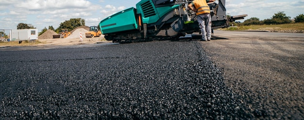 I lavoratori stradali con le pale in mano lanciano asfalto biforcuto su una nuova strada Riparazioni del servizio stradale th