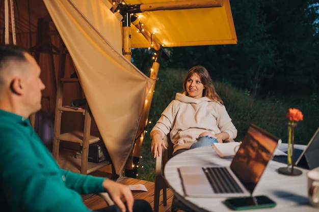 I liberi professionisti della coppia felice della famiglia si riposano dopo aver lavorato al laptop su un'accogliente tenda glamping in serata estiva Tenda da campeggio di lusso per vacanze all'aperto e vacanze Concetto di stile di vita