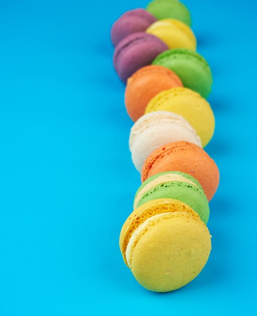 I macarons cotti multicolori rotondi con crema si trovano in una linea su un fondo blu