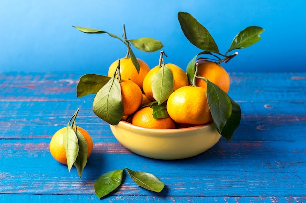 I mandarini maturi arancio o i mandarini fruttificano con le foglie verdi, sopra fondo di legno blu rustico.