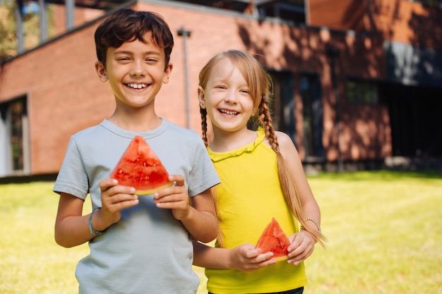 I migliori amici di sempre. Allerta bambini affascinanti che sorridono e mangiano un'anguria matura