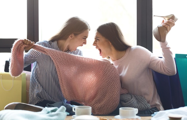 I migliori amici sono in conflitto. Due ragazze che discutono del maglione che hanno comprato, sullo sfondo del caffè