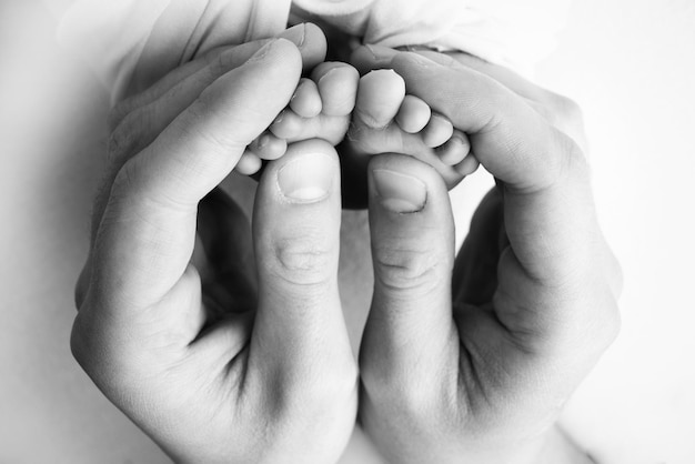 I palmi dei genitori Un padre e una madre tengono un neonato per le gambe I piedi di un neonato nelle mani dei genitori Foto dei talloni e delle dita del piede Fotografia macro in studio in bianco e nero