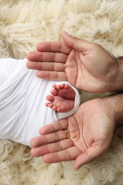 I palmi del padre la madre stanno tenendo il piede del neonato in una coperta bianca I piedi del neonato sui palmi dei genitori Studio macro foto delle dita dei piedi e dei tacchi di un bambino