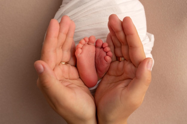 I palmi del padre, la madre tengono i piedi del neonato in una coperta bianca. Piedi del neonato sui palmi dei genitori. Fotografia in studio delle dita dei piedi, dei talloni e dei piedi di un bambino.