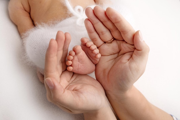 I palmi del padre, la madre tengono il piede del neonato. Piedi del neonato sui palmi dei genitori. Fotografia in studio delle dita dei piedi, dei talloni e dei piedi di un bambino. Concetto.