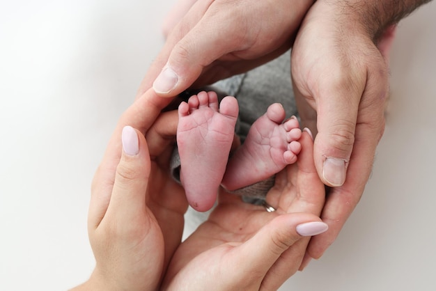 I palmi del padre la madre tiene il piede del neonato su sfondo bianco Piedi del neonato sui palmi dei genitori Fotografia di un bambino dita dei piedi talloni e piedi