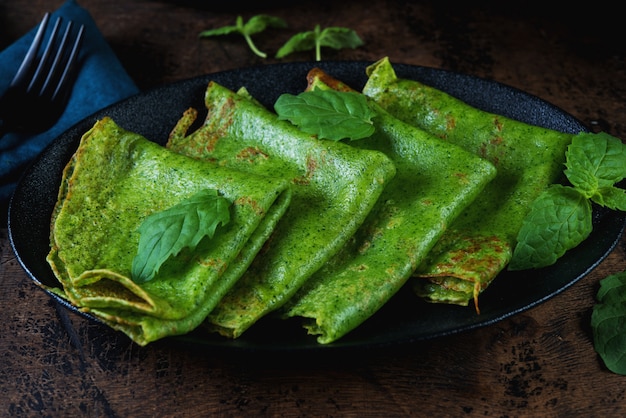 I pancake sottili degli spinaci sono verdi su una tavola di legno. Foto orizzontale.