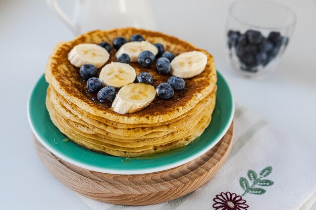 I pancake sul mucchio sono ricoperti di miele di mirtilli e fette di banana sul piatto Sano gustoso