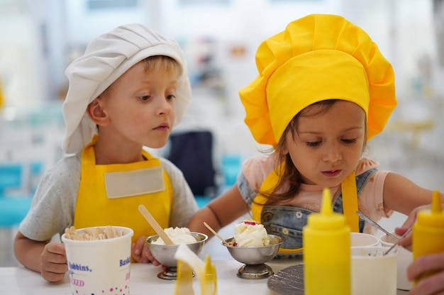 I piccoli bambini caucasici giocano a bambini chef con un grembiule e un cappello da chef