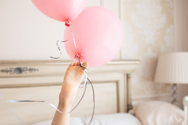 I piccoli piedi creativi del bambino tengono il mazzo di palloncini rosa compleanno Interno beige Casa in colori chiari