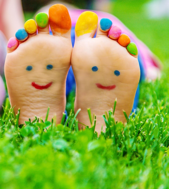 I piedi dei bambini con un motivo di vernici sorridono sull'erba verde Messa a fuoco selettiva