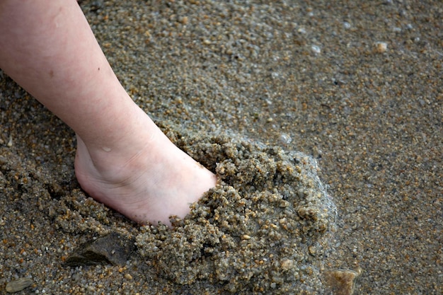 I piedi del bambino nel primo piano della sabbia.