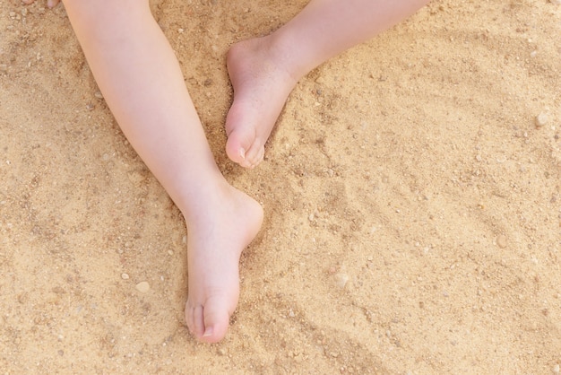 I piedi del bambino su uno sfondo di sabbia