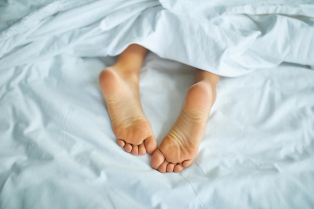 I piedi della ragazza ricoperti da un lenzuolo bianco, che dorme in un letto comodo, Focus sul piede, sonno sano dei bambini