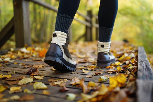 I piedi delle donne con gli stivali percorrono un sentiero in legno nella foresta autunnale