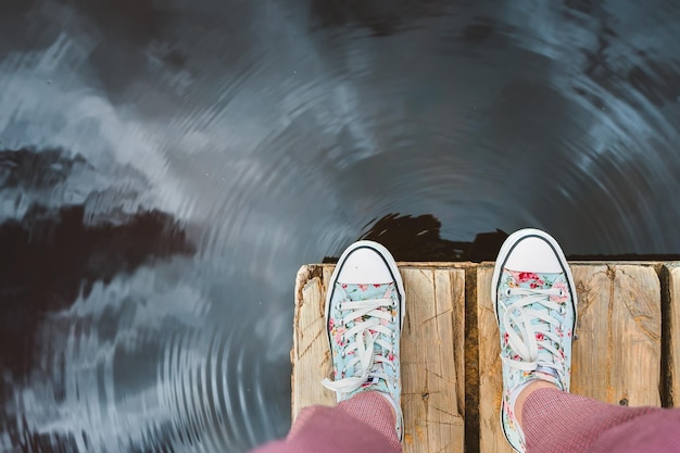 I piedi delle donne stanno su un molo di legno una ragazza in scarpe da ginnastica si sta riposando sul lago