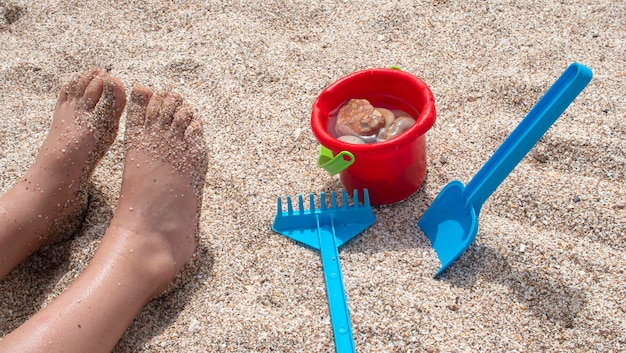 I piedi di un bambino pieni di sabbia che giocano con pale e secchi di plastica sulla spiaggia